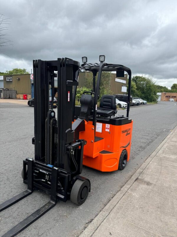 The Bendi Eco B40 Battery Electric Sideloading Articulated Forklift Truck, in orange, is parked on a paved outdoor area. Overhead, the sky is cloudy, and industrial buildings are visible in the background. The forklift has a black lifting mechanism and an open driver’s seat.