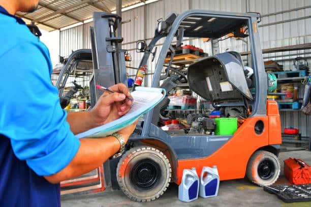A mechanic, clipboard in hand, diligently conducts a forklift servicing with its engine cover open in the workshop. Nearby, two containers of engine oil sit ready for use, while shelves filled with tools and equipment line the background.